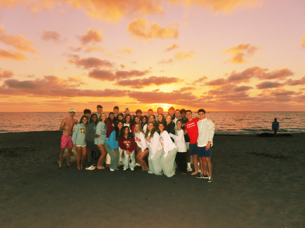Members of the Class of 2025 pose for a group picture on the beach as the sun
rises over the horizon.